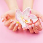 Females hands with pastel manicure are holding an orchid flower. Pink background