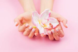 Females hands with pastel manicure are holding an orchid flower. Pink background